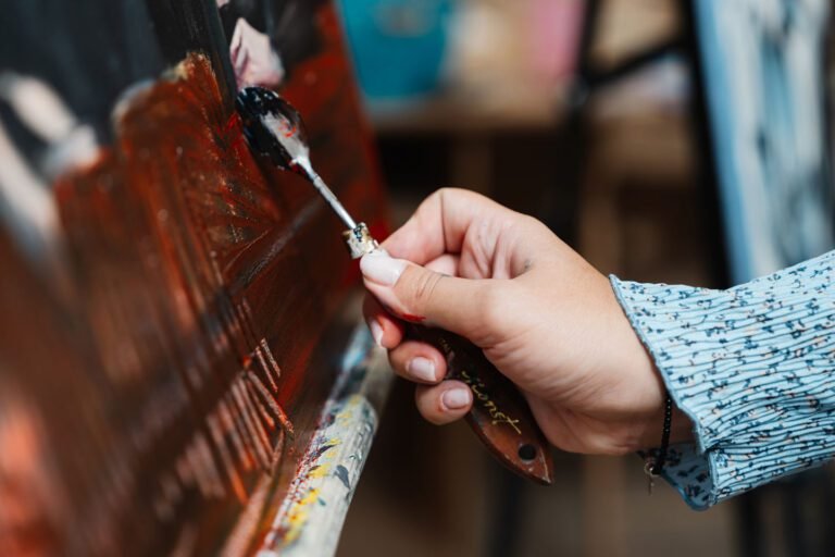 Artist applying black paint to canvas in brightly lit studio during daytime