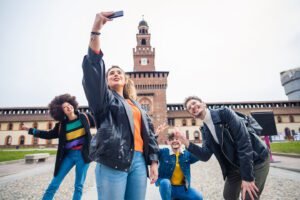 Group of four people taking selfie in front off Sforzesco castle in Milan - tourism, sociable, sightseeing concept