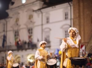 Performers in traditional attire playing drums at a festive night event.