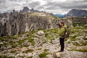 Photographer shoots mountain scene with his camera. Man with trekking clothes and photographic equipment with raincoat and backpack.